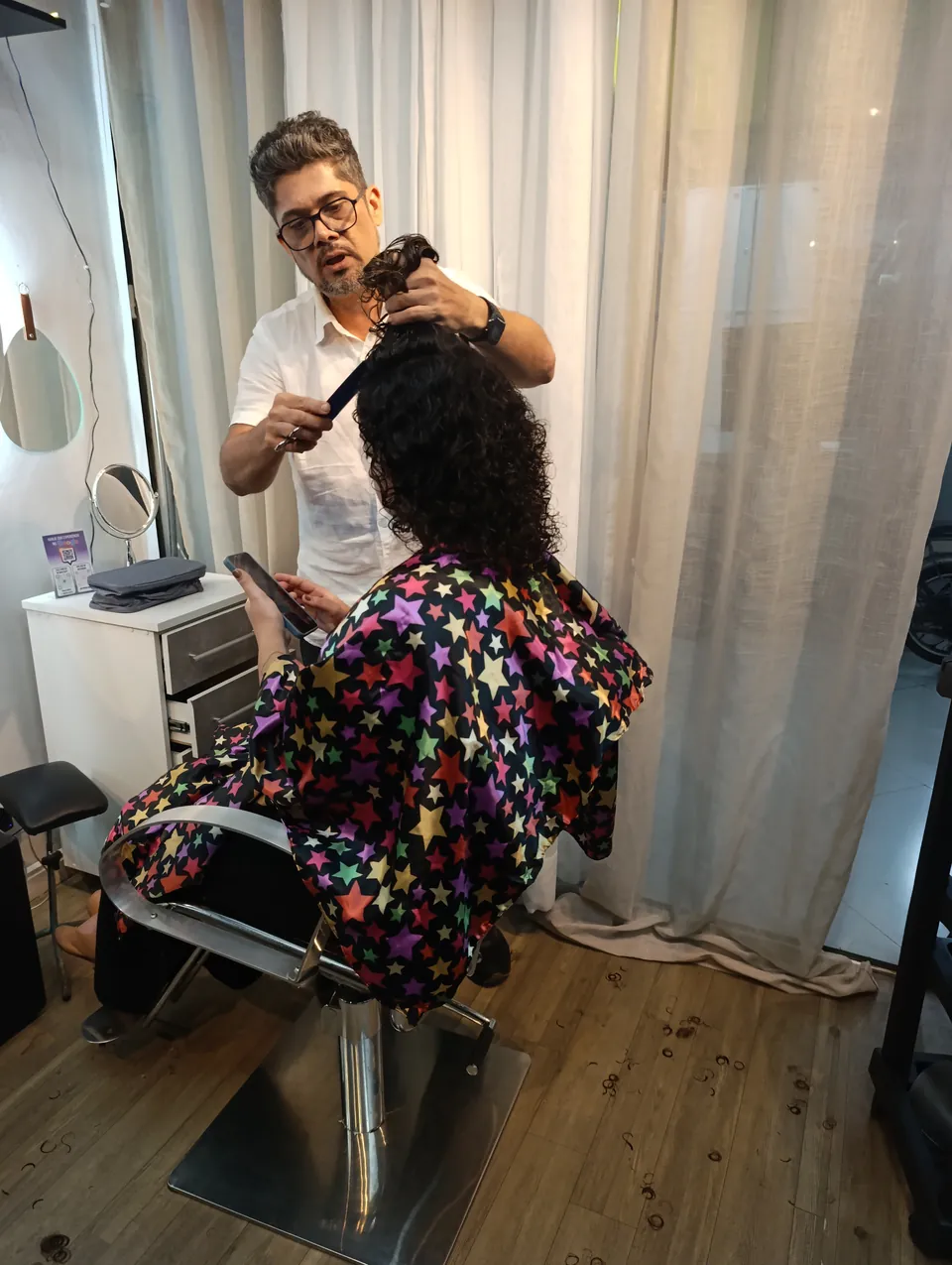Pablo corta o cabelo cacheado da mesma cliente, com tesoura e pente
