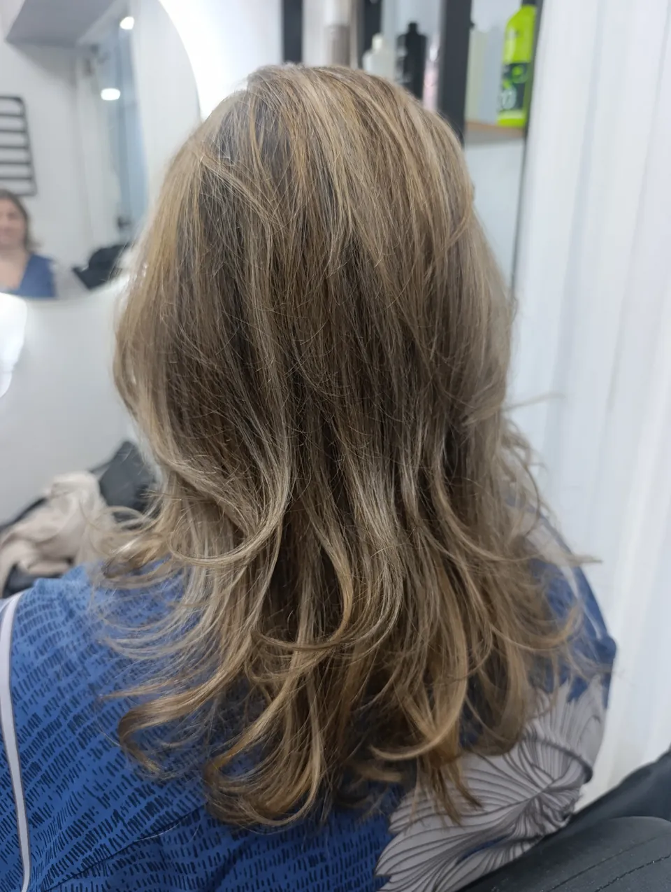 Mechas bege em corte repicado médio, de costas, com o rosto da cliente refletido no espelho