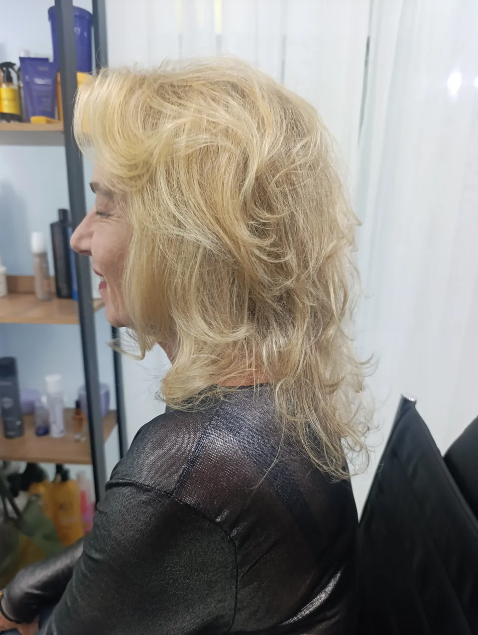 Cliente de perfil, sorrindo, com corte repicado em loiro claro