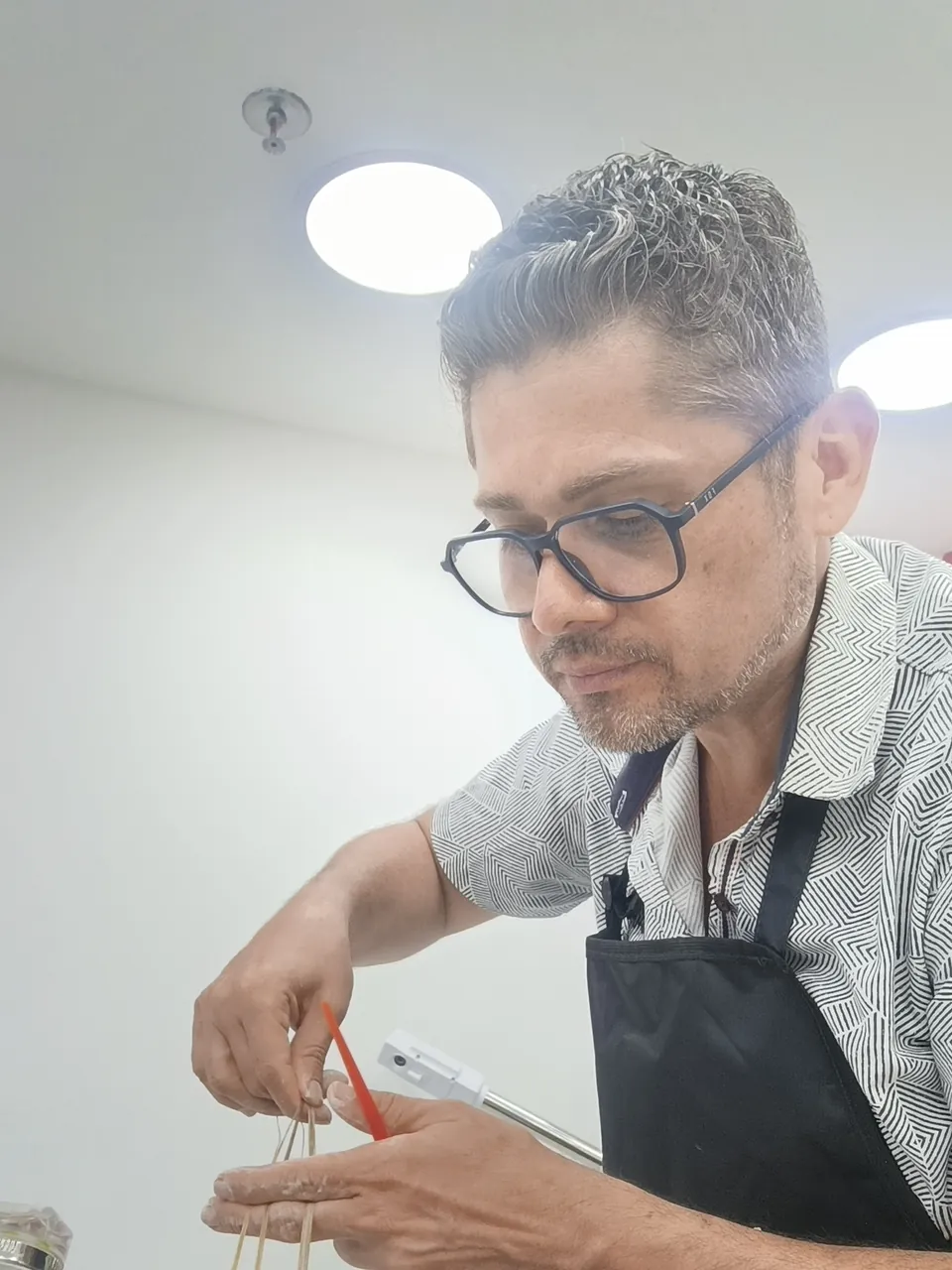 Pablo Roco, de óculos e avental preto, separa com atenção mechas finas de uma cliente durante uma coloração