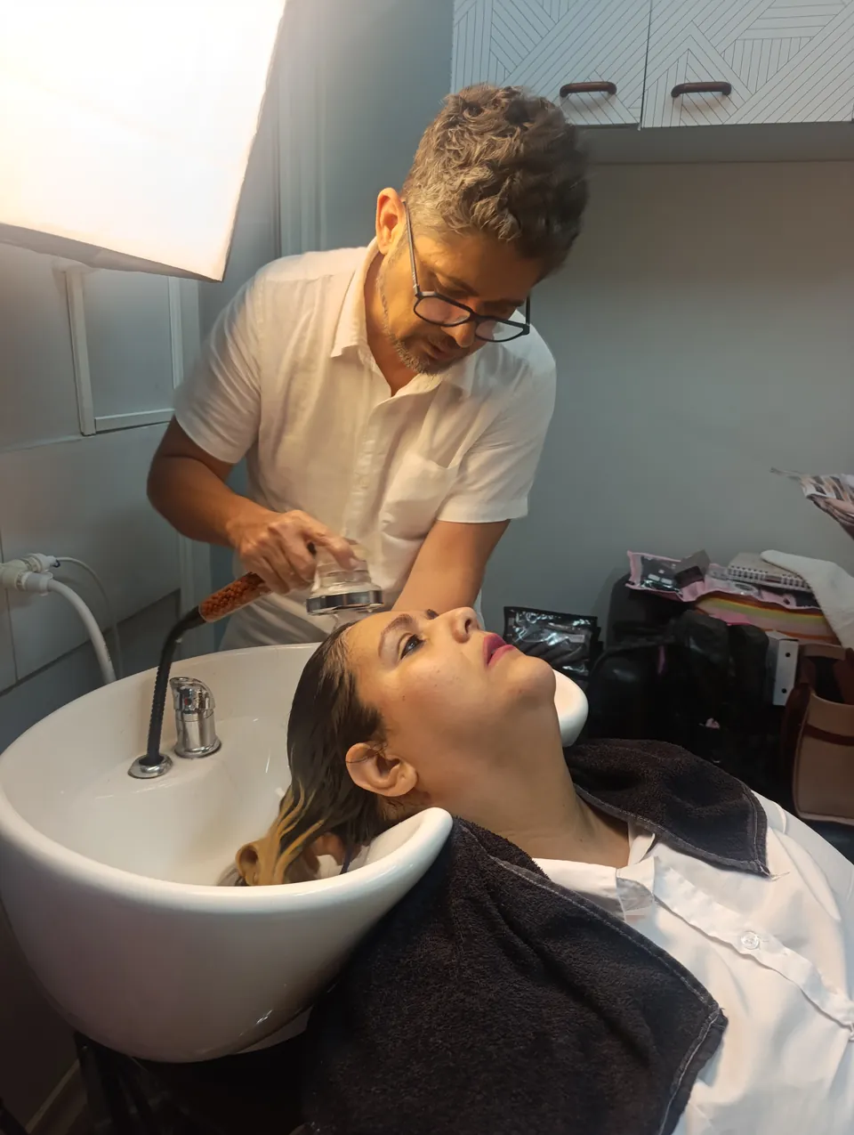 Pablo cuida do cabelo de uma cliente reclinada no lavatório